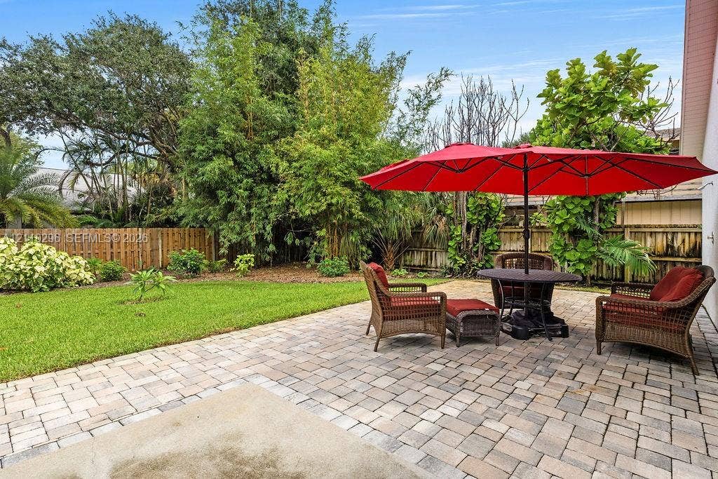 Backyard featuring a paved stone patio, manicured lawn, wood privacy fencing, and mature trees