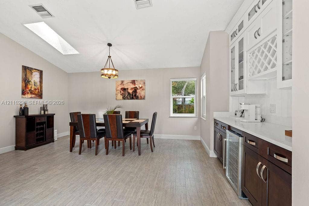 Dining area featuring wood-finish tile flooring, vaulted ceilings with a skylight, built-in cabinetry with glass-front uppers and wine storage, and a dedicated beverage refrigerator