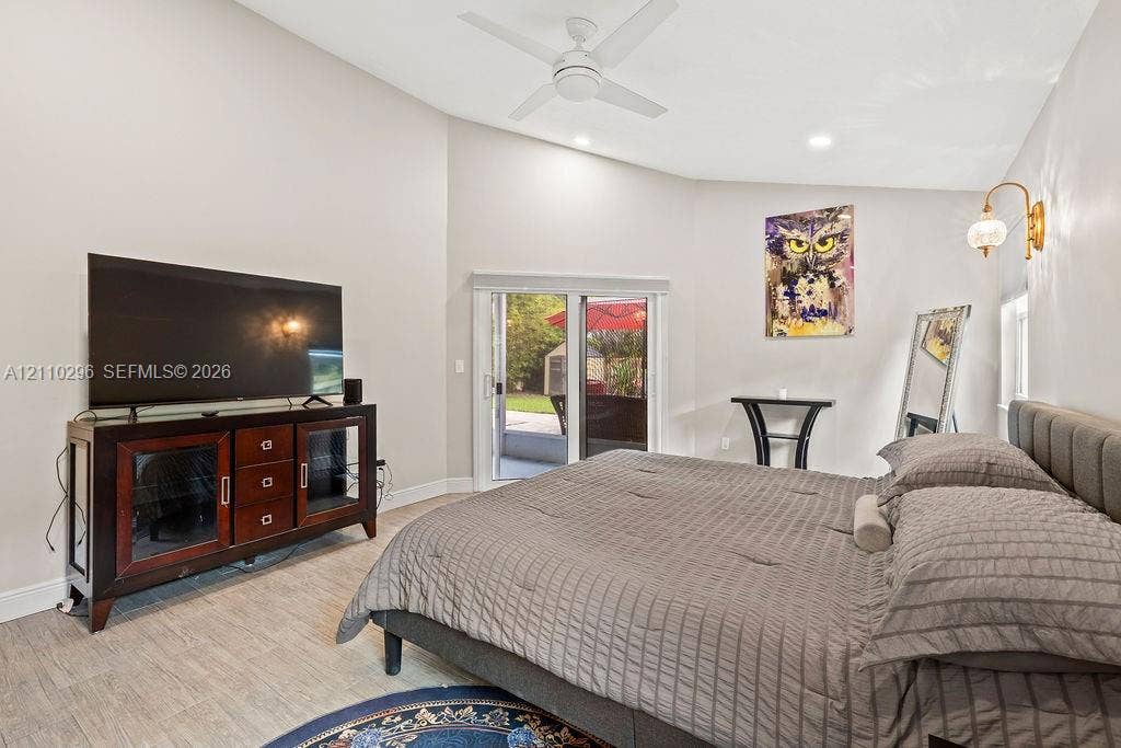 Vaulted ceilings, wood-finish tile flooring, ceiling fan, sliding glass door, and wall-mounted sconce lighting