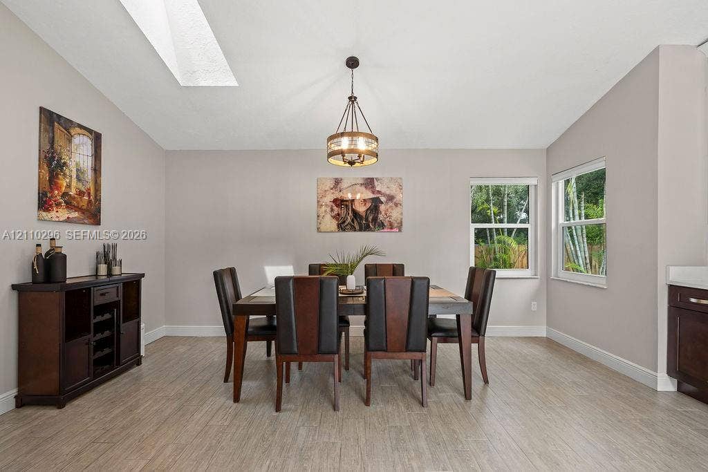 Vaulted ceiling with skylight, neutral wall tones, wood-finish flooring, and a multi-light drum pendant fixture