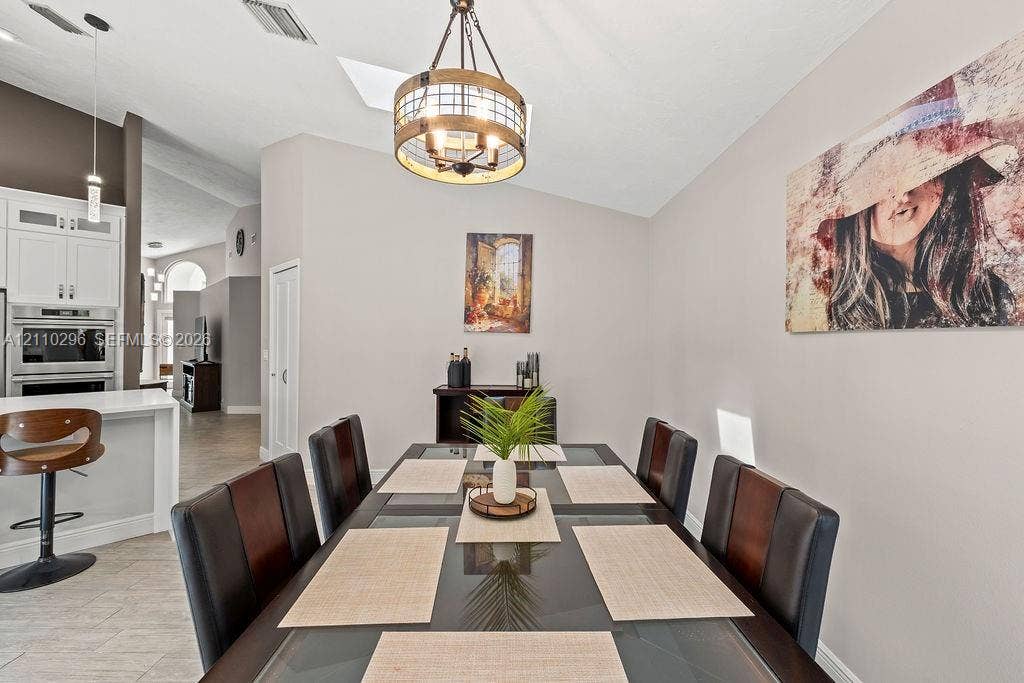 Vaulted ceiling featuring a skylight, drum-style wood and metal chandelier, neutral wall tones, and ceramic tile flooring