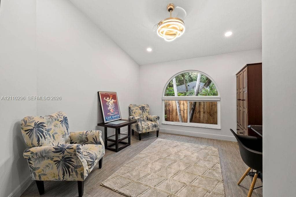 Room featuring wood-finish flooring, vaulted ceilings, a prominent arched window, recessed lighting, and a modern gold-finish ceiling fan with integrated illumination