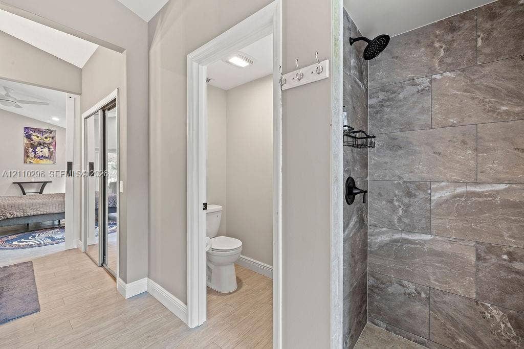 Shower featuring large-format stone-patterned tile, matte black shower head and plumbing fixtures, wood-finish flooring, and mirrored sliding closet doors
