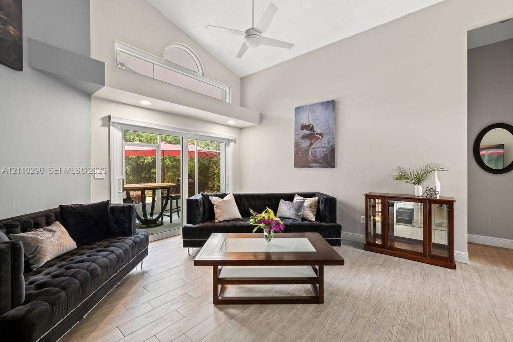 Vaulted ceiling featuring a central fan, ceramic tile flooring, sliding glass door, and an arched transom window