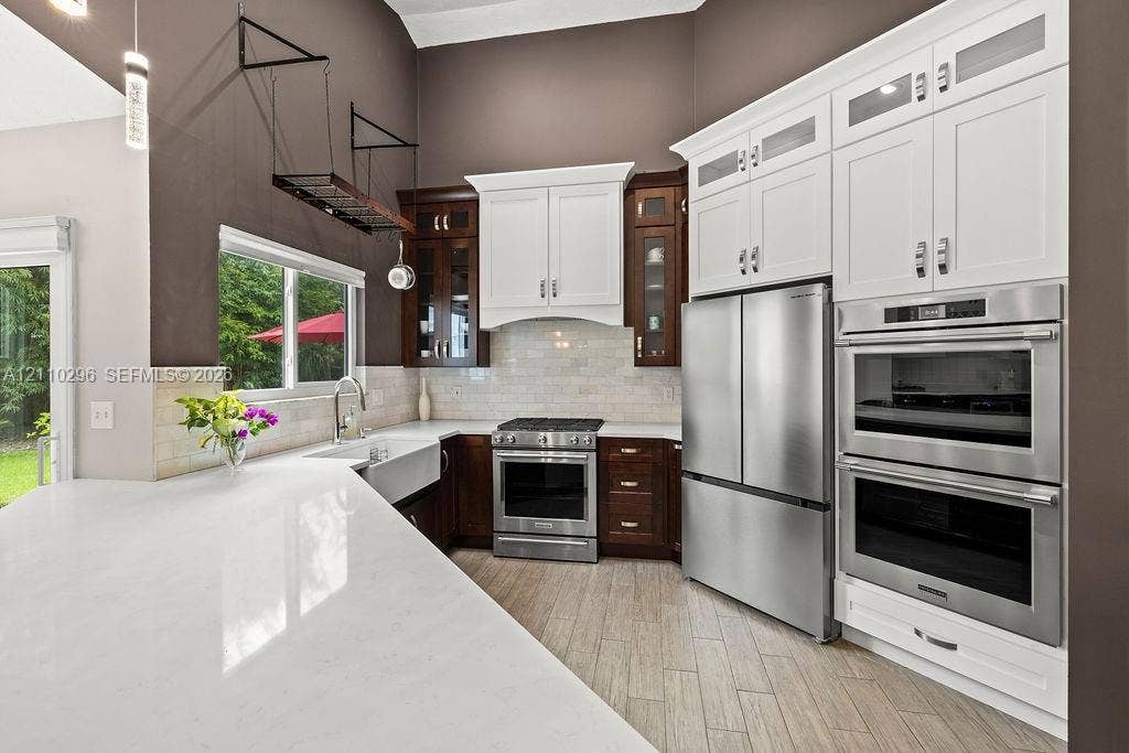 Kitchen featuring a stone-surface island, apron-front sink, stainless steel built-in double wall ovens, two-tone cabinetry, and wood-finish tile flooring