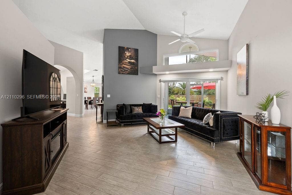 Living area featuring vaulted ceilings, wood-finish tile flooring, a neutral color palette with an accent wall, sliding glass doors, and a ceiling fan