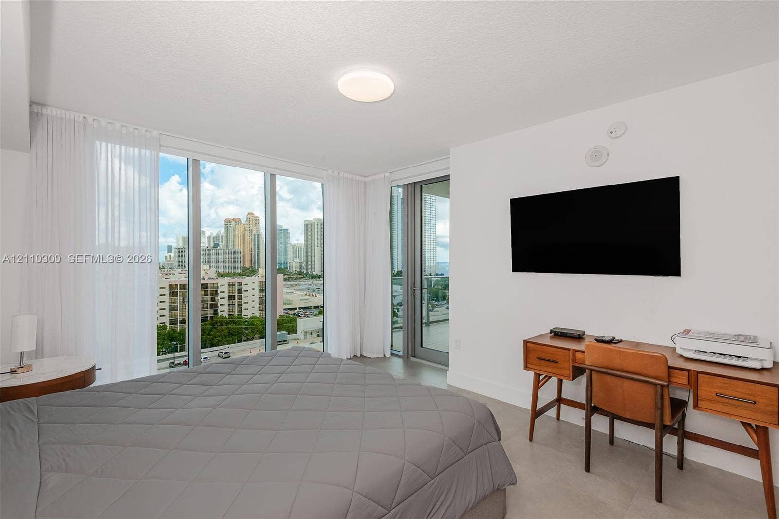 Master Bedroom. Floor-to-ceiling windows, city skyline backdrop, flush-mount lighting, and glass door access to an exterior balcony