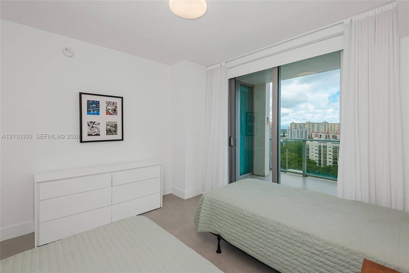 Bedroom 2. Floor-to-ceiling glass sliding doors, private balcony, neutral large-format tile flooring, and flush-mount ceiling lighting