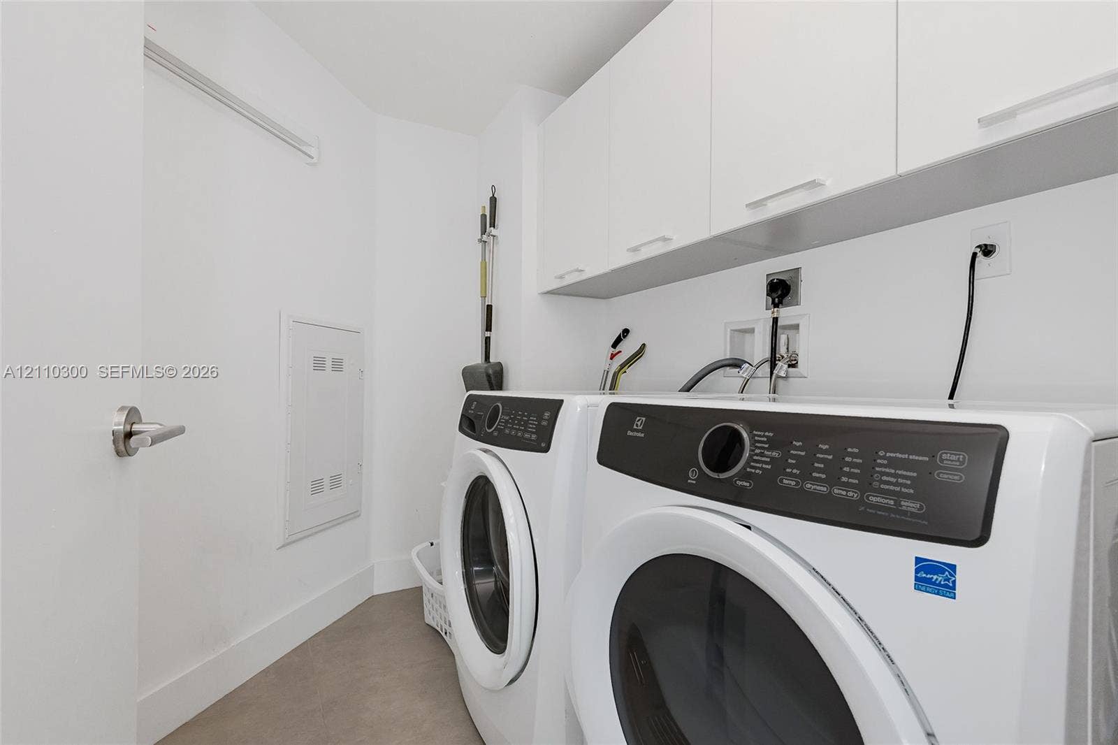 Laundry area featuring custom white upper cabinetry, stainless steel-trimmed appliances, and smooth-finish flooring