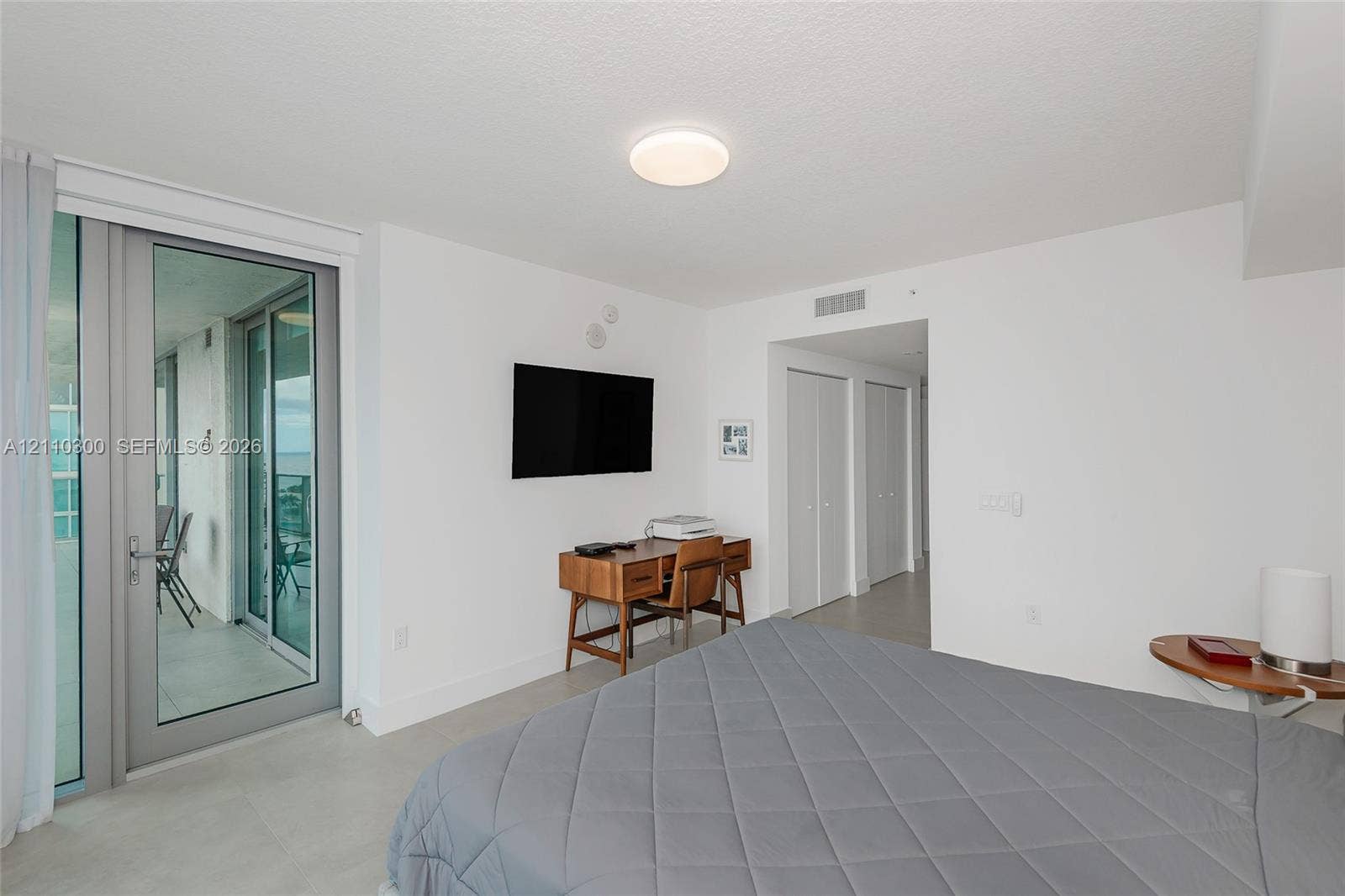 Master Bedroom. Neutral-toned tile flooring, large sliding glass door with access to a balcony, and dual bi-fold closet doors