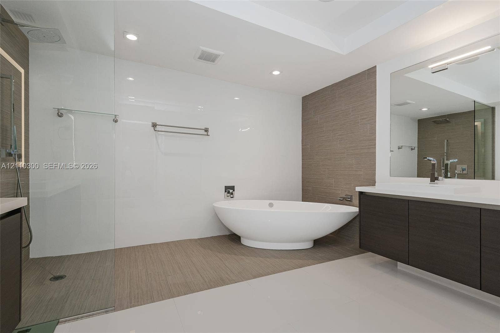 Master Bathroom Freestanding soaking glass-enclosed walk-in shower, wall-mounted dark wood-finish cabinetry with quartz countertop, and recessed lighting