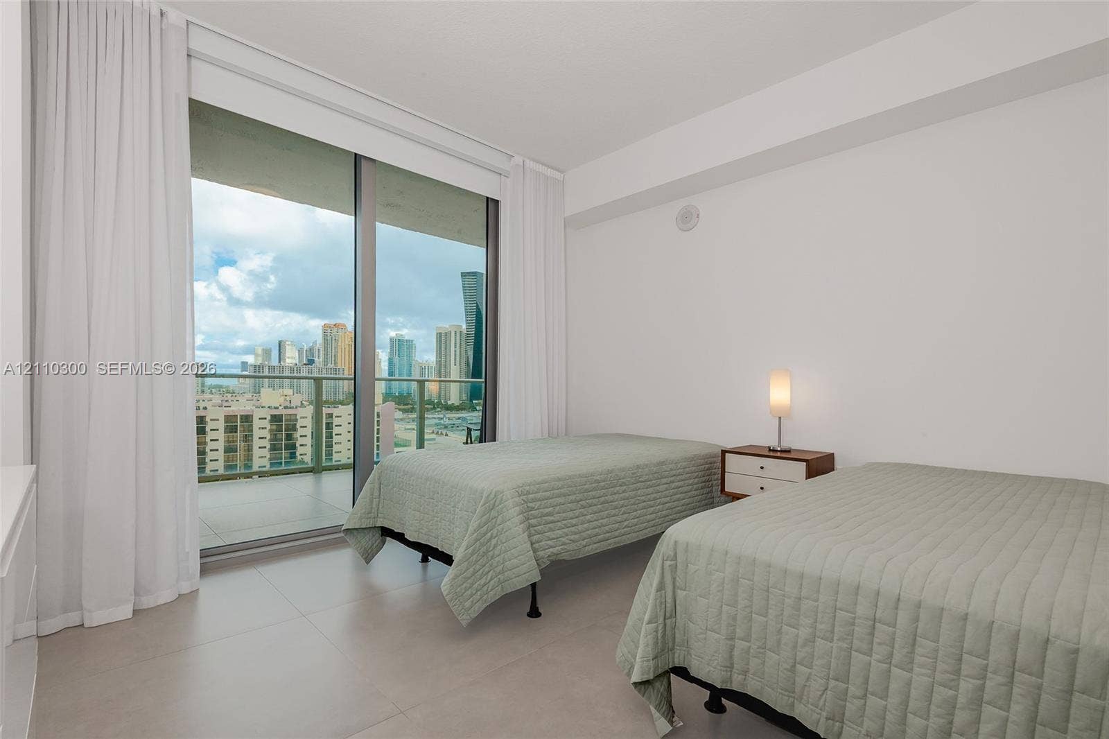 Bedroom 2. Floor-to-ceiling sliding glass door, private balcony, large format tile flooring, and urban skyline backdrop
