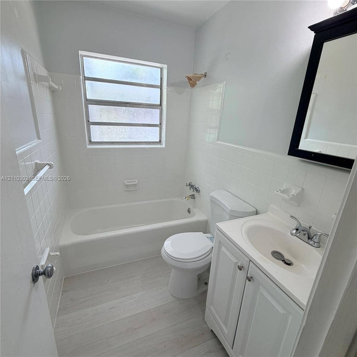 Bathroom featuring wood-finish flooring, white tile wall surround, built-in soaking tub, and vanity with an integrated basin and chrome hardware