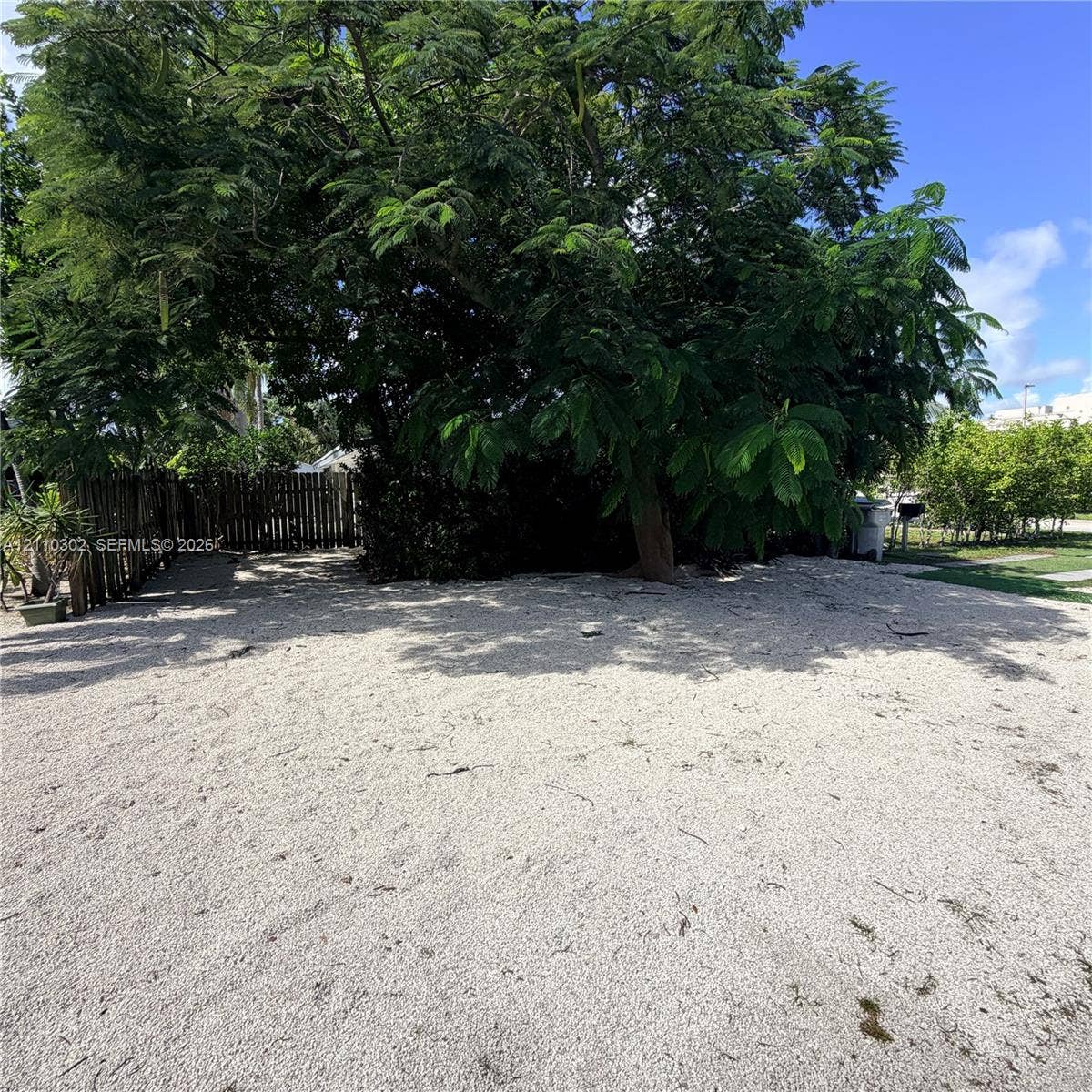 Expansive level lot featuring gravel ground cover, mature tree canopy, and a wood picket fence perimeter