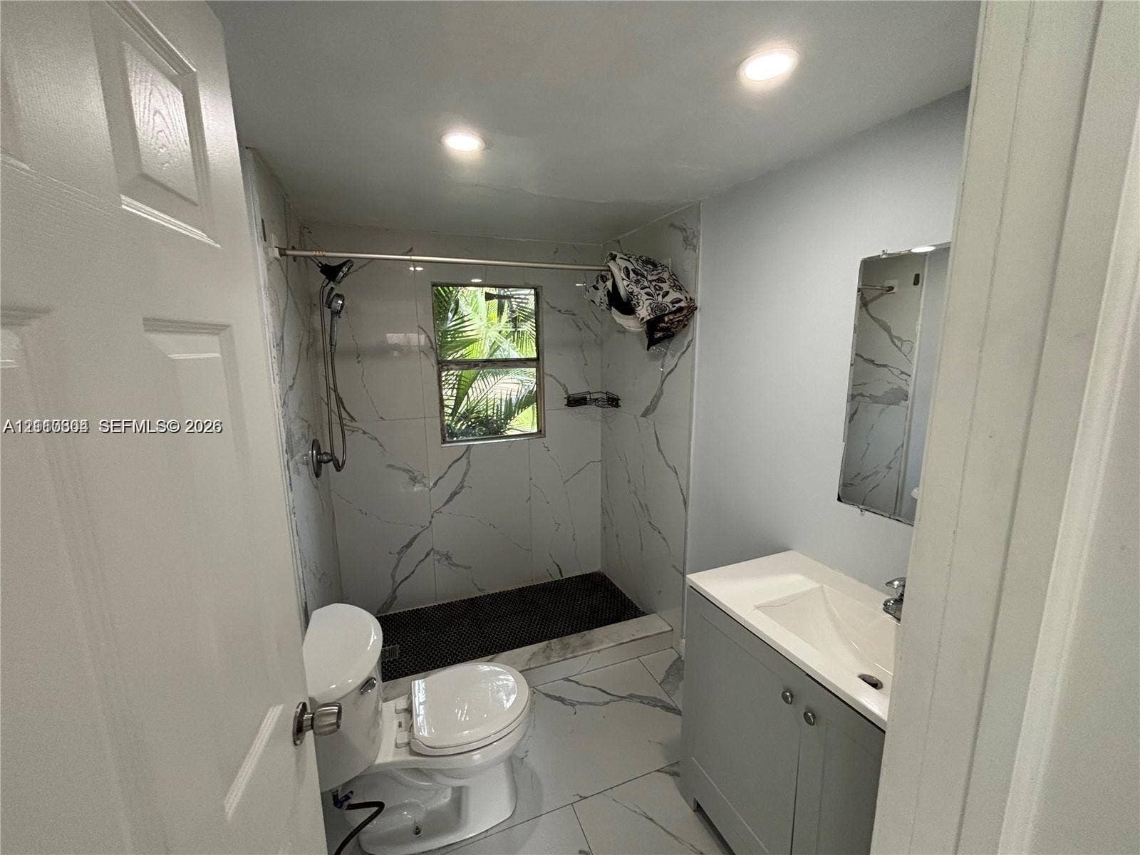 729 NW 19th Avenue, Fort Lauderdale, FL 33311 Bathroom featuring large-format stone-patterned tile, walk-in shower with rainfall showerhead, vanity with integrated sink, and recessed lighting
