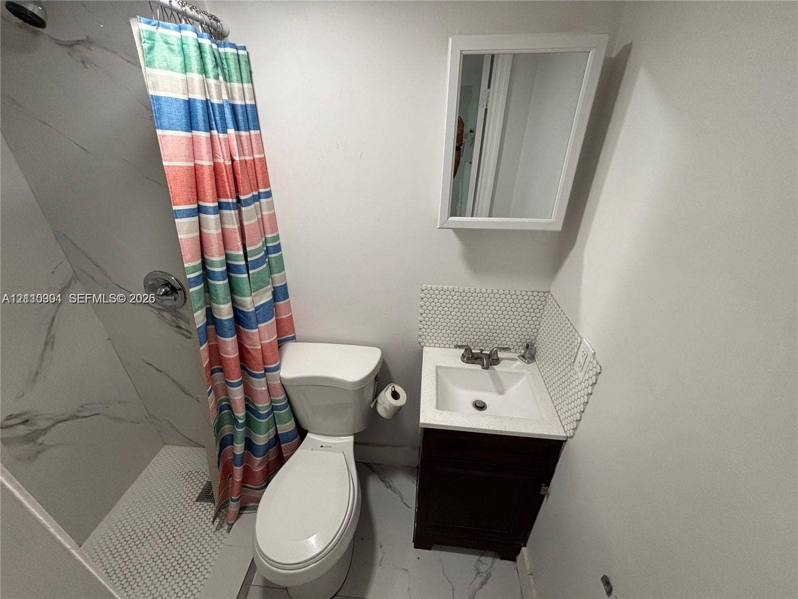 729 NW 19th Avenue, Fort Lauderdale, FL 33311 Shower with stone-finish wall tile, vanity cabinet featuring a solid surface countertop, hex-tile backsplash, and wall-mounted medicine cabinet