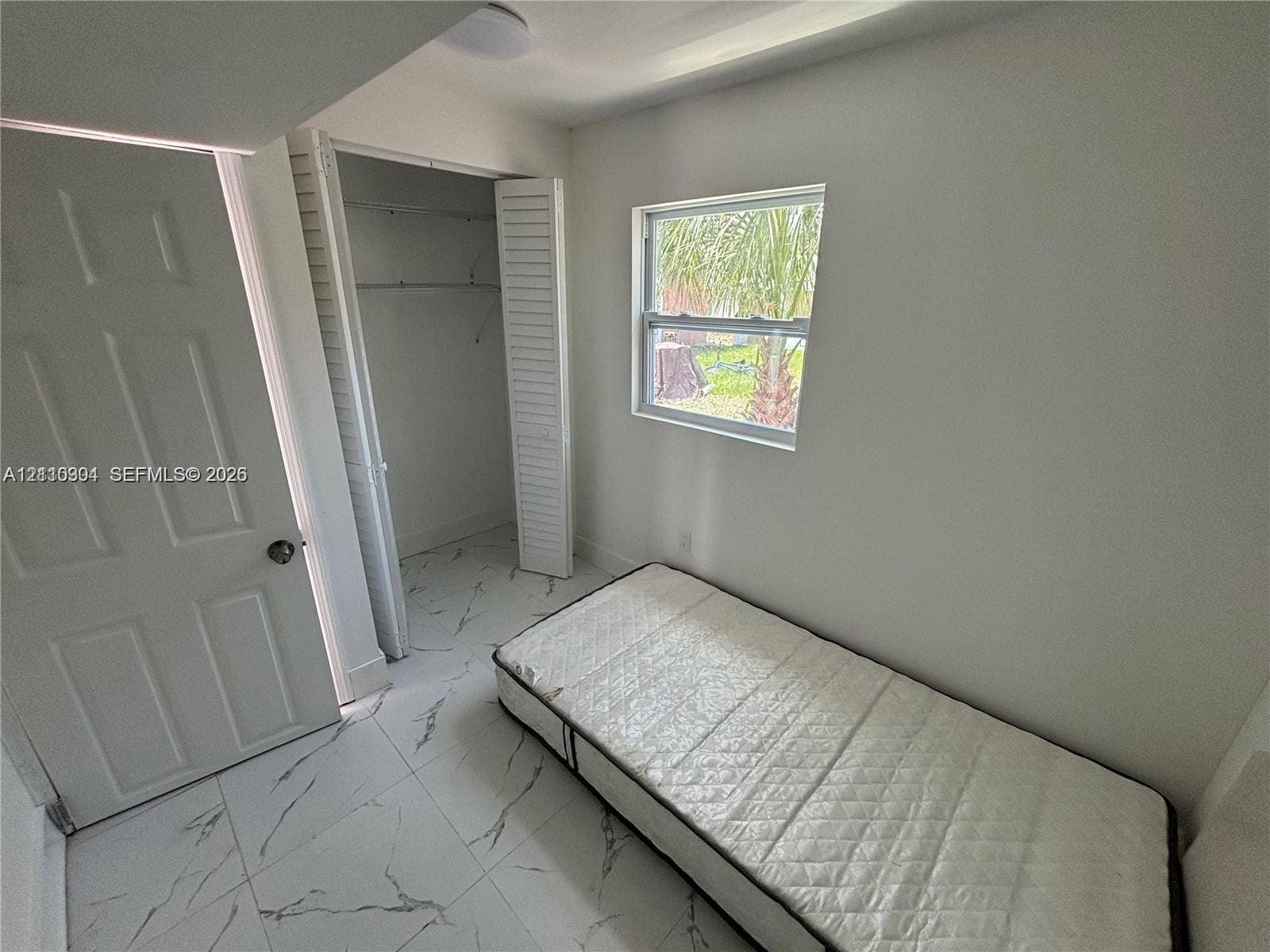 729 NW 19th Avenue, Fort Lauderdale, FL 33311 Neutral-toned room featuring large-format tile flooring with marbling detail, single-pane window, and closet with louvered double doors