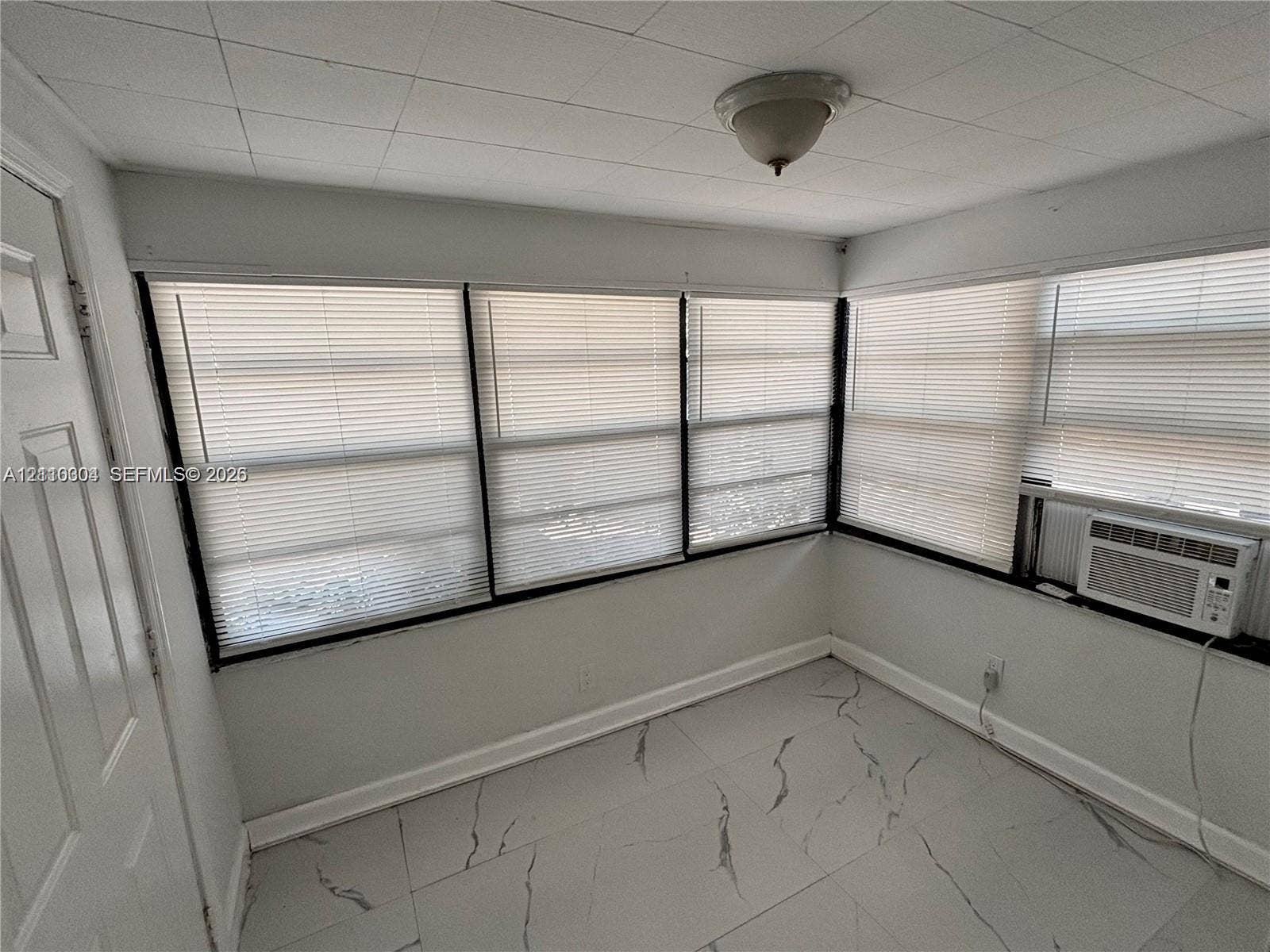 729 NW 19th Avenue, Fort Lauderdale, FL 33311 Large-format stone-pattern tile flooring, multiple windows with integrated blinds, and an installed wall-mounted air conditioning unit