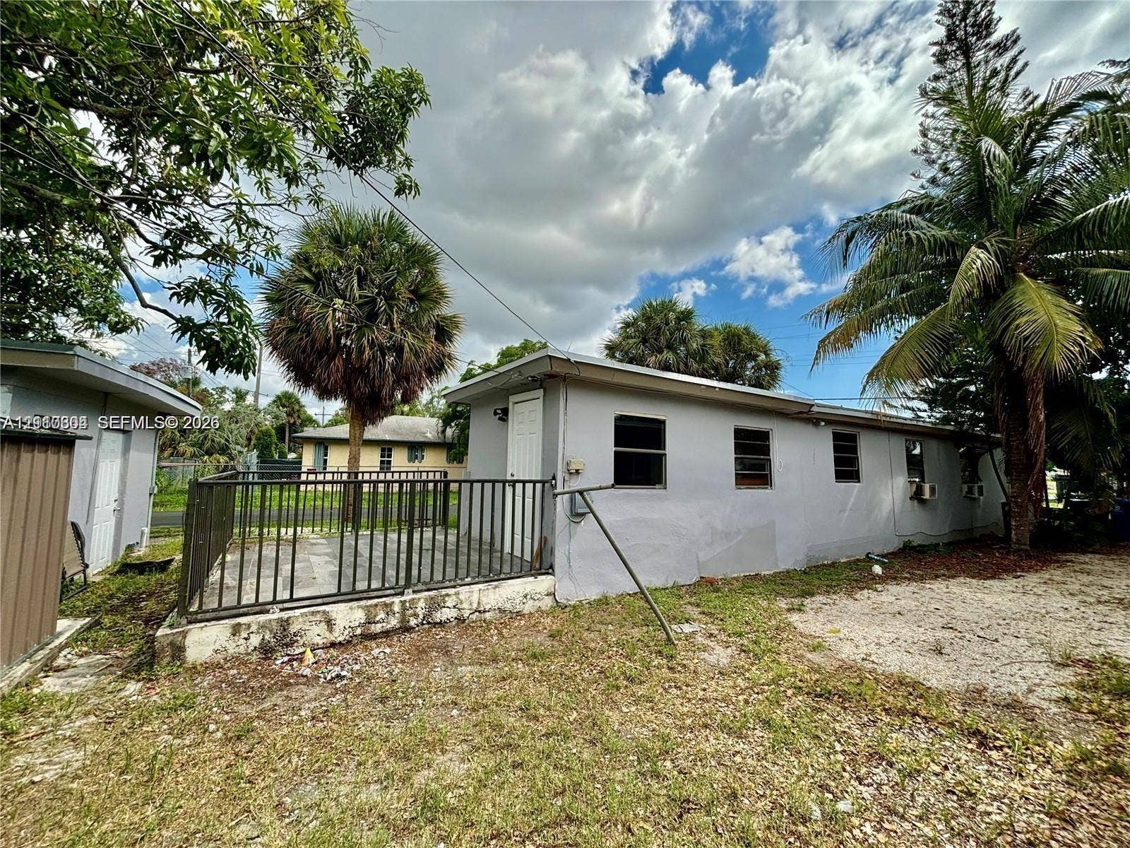 729 NW 19th Avenue, Fort Lauderdale, FL 33311 Exterior space featuring a concrete patio enclosed by metal fencing, neutral-toned stucco siding, and mature palm trees