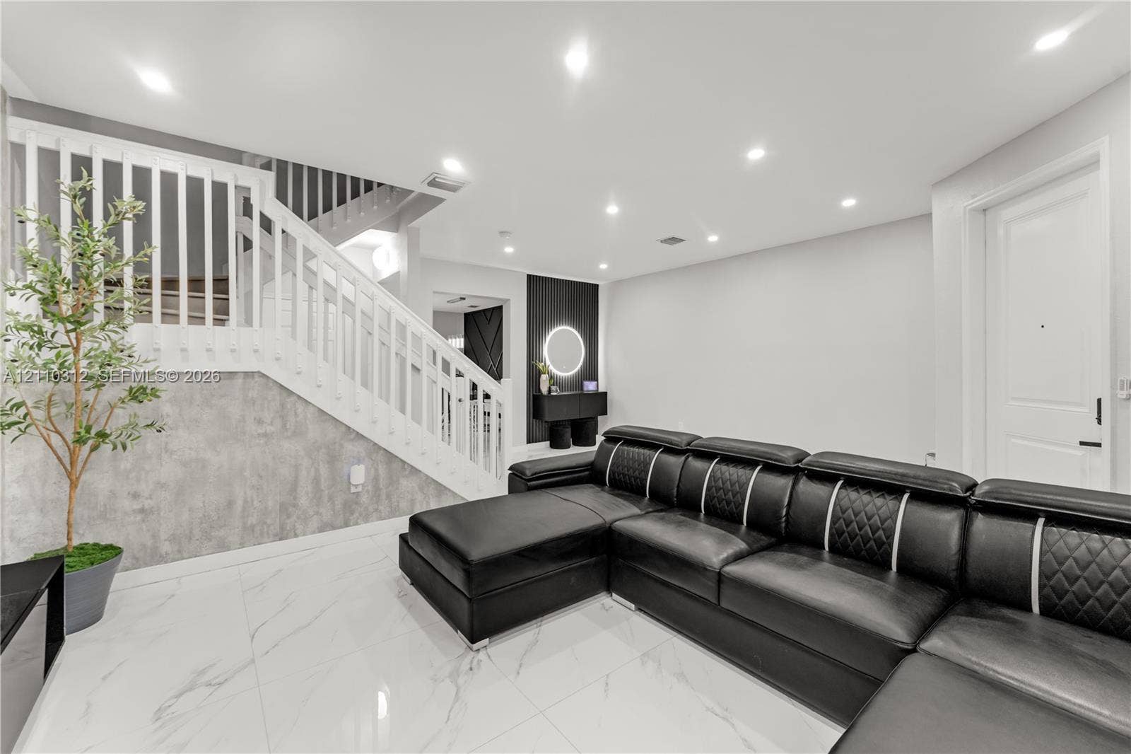 11524 SW 248th Lane, Homestead, FL 33032 Polished tile flooring, recessed lighting, white wood-slat staircase railing, gray stone-finish wall paneling, and a circular LED wall fixture