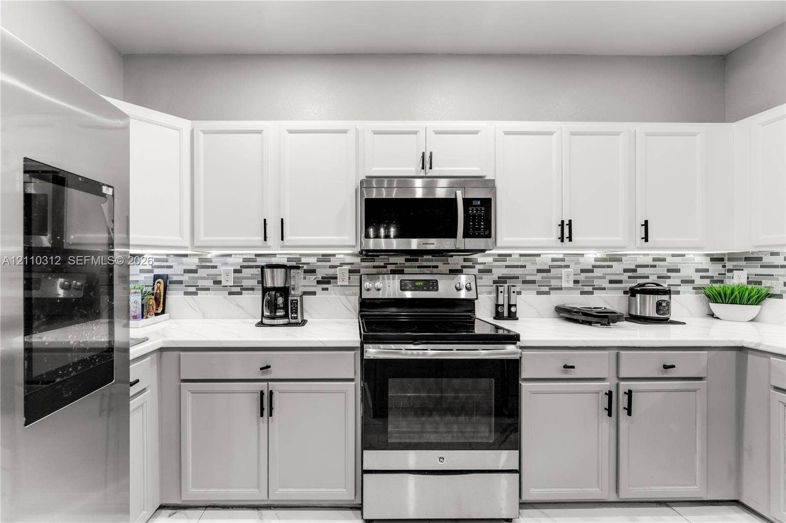 11524 SW 248th Lane, Homestead, FL 33032 Kitchen featuring white shaker-style cabinetry, solid-surface countertops, a multi-tone glass tile backsplash, and stainless steel appliances