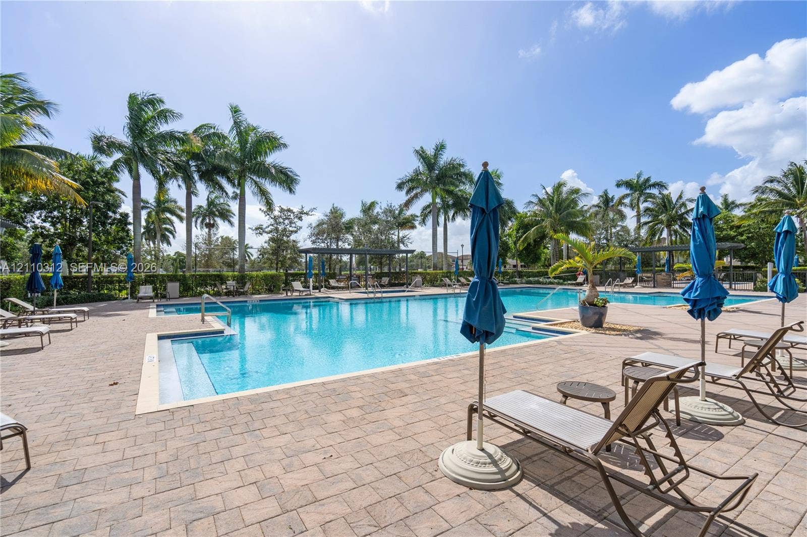 11524 SW 248th Lane, Homestead, FL 33032 Swimming pool featuring a paver deck, shallow entry shelf, and integrated covered structures, surrounded by manicured landscaping and mature palms