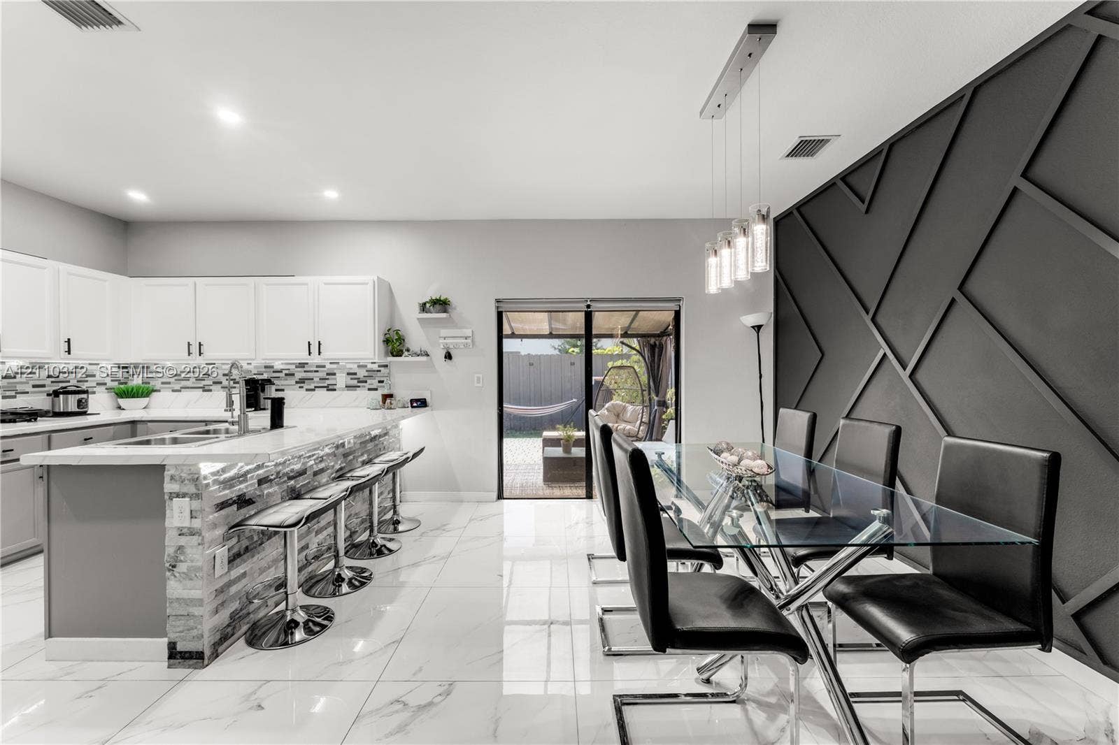 11524 SW 248th Lane, Homestead, FL 33032 Kitchen featuring white cabinetry, stone-finish countertops, a multi-textured stone backsplash, glossy tile flooring, and an accent wall with geometric millwork