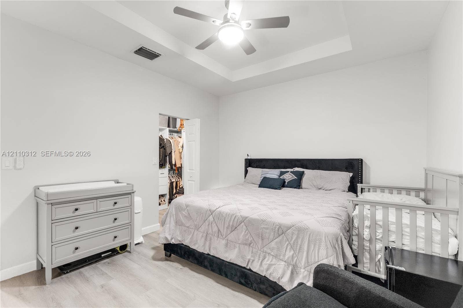 11524 SW 248th Lane, Homestead, FL 33032 Tray ceiling featuring a central light-integrated ceiling fan, neutral wall finishes, wood-finish flooring, and a walk-in closet with built-in shelving