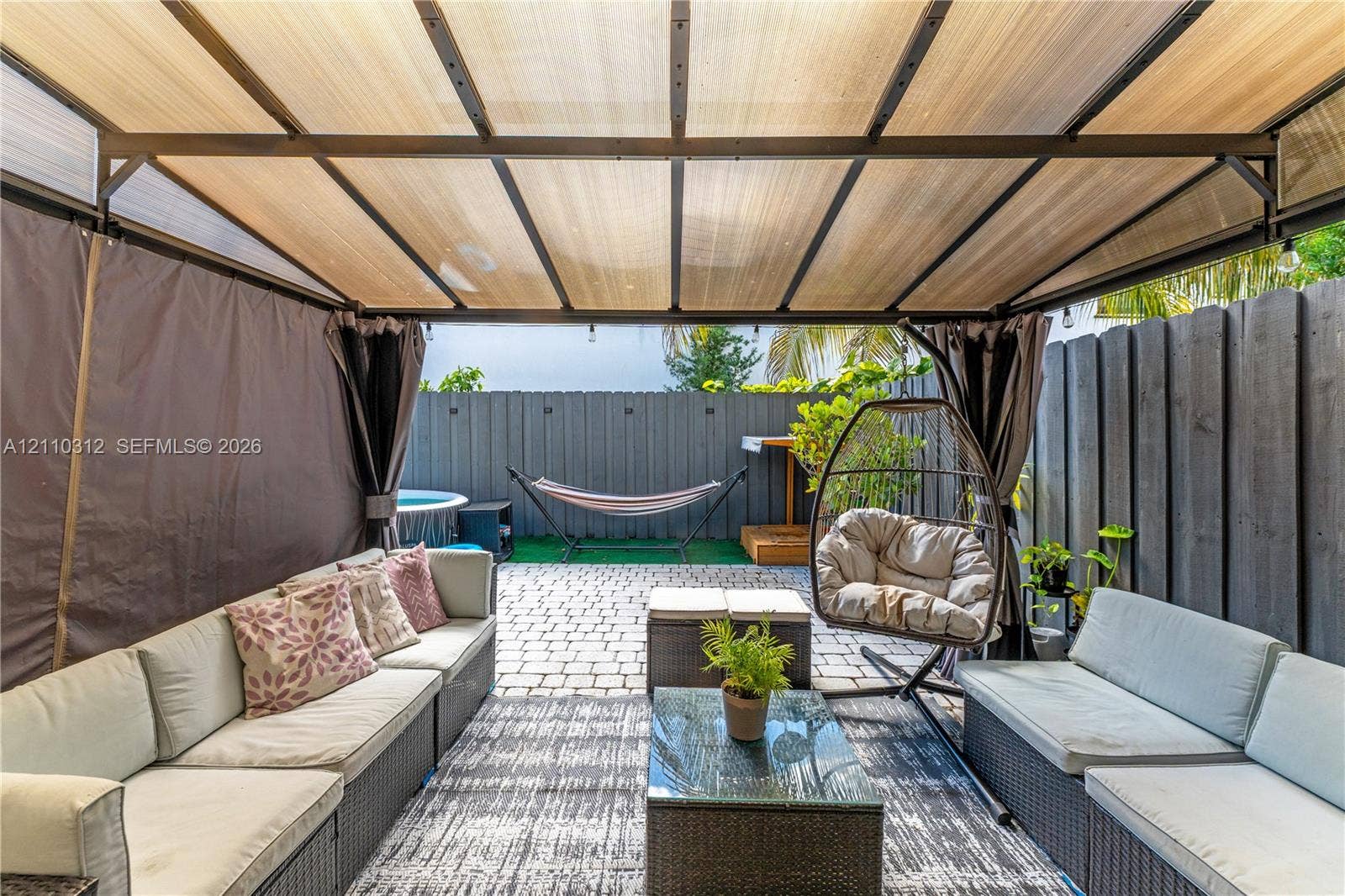11524 SW 248th Lane, Homestead, FL 33032 Outdoor living space featuring a metal-frame pavilion with a semi-transparent roof, paver patio, and full-perimeter vertical wood fencing