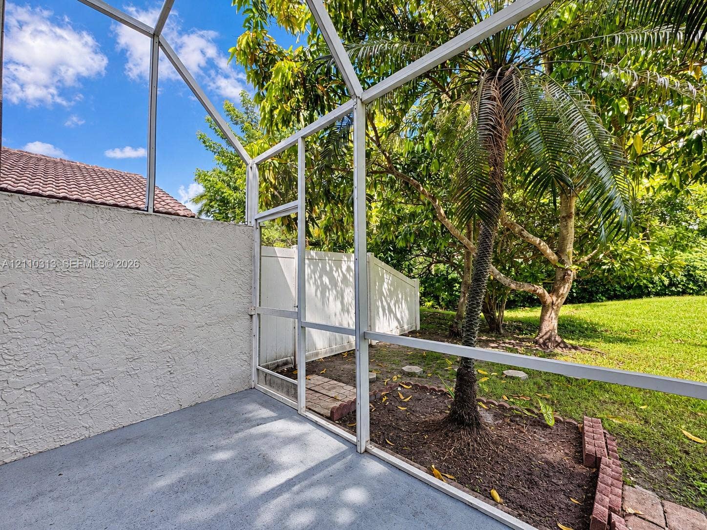 17731 SW 23rd Street, Miramar, FL 33029 Screened-in patio featuring a concrete floor, stucco wall, white aluminum framing, and direct access to a grassy yard with mature palms and vinyl privacy fencing