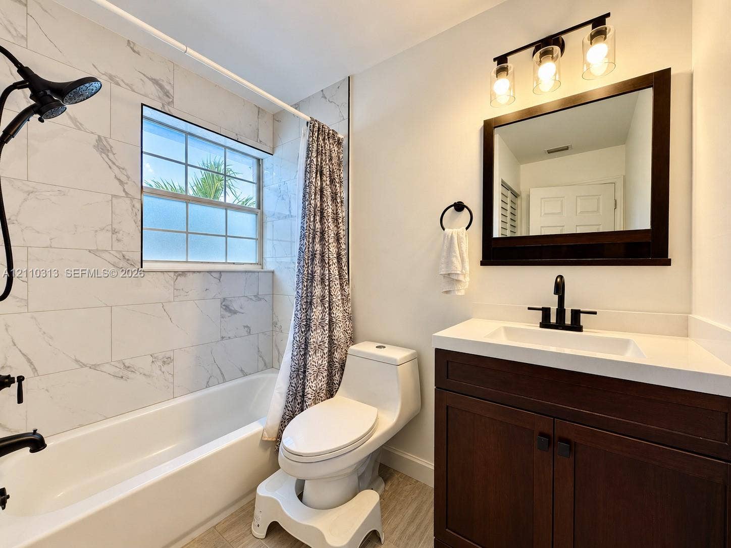 17731 SW 23rd Street, Miramar, FL 33029 Bathroom featuring a vanity with a white countertop, matte black faucet, wall-mounted mirror, three-light fixture with glass shades, and tub surround tiled in a stone-pattern finish