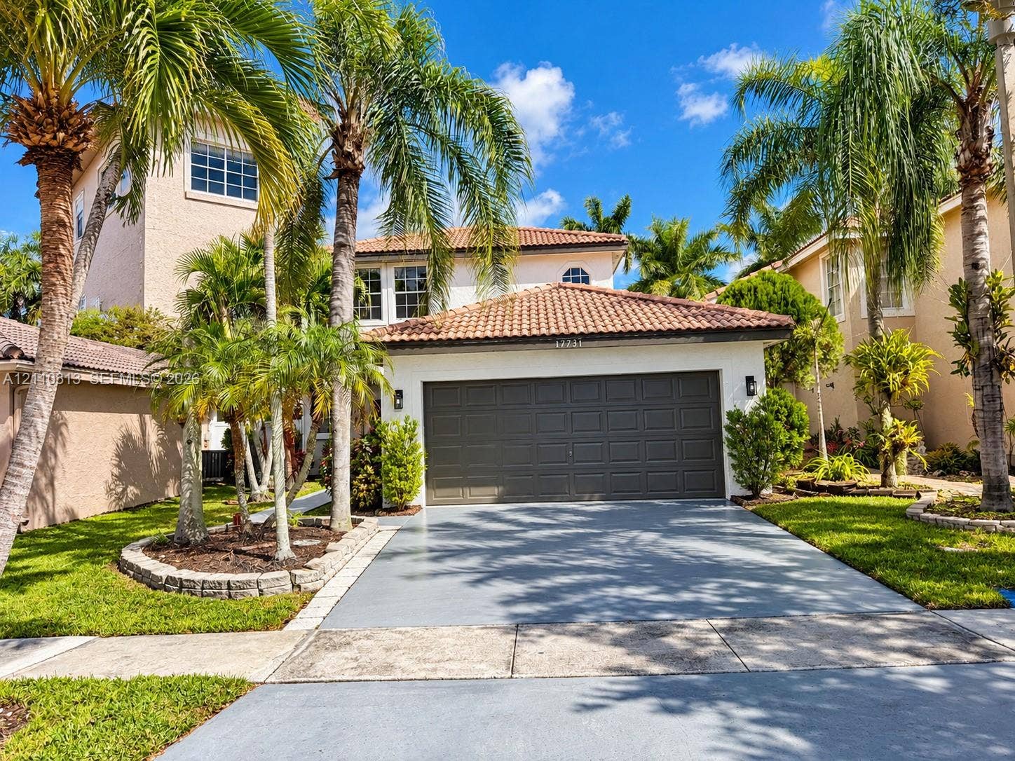 17731 SW 23rd Street, Miramar, FL 33029 Two-story exterior featuring a tile roof, neutral stucco finish, paneled garage door, concrete driveway, and established palm landscaping with stone edging