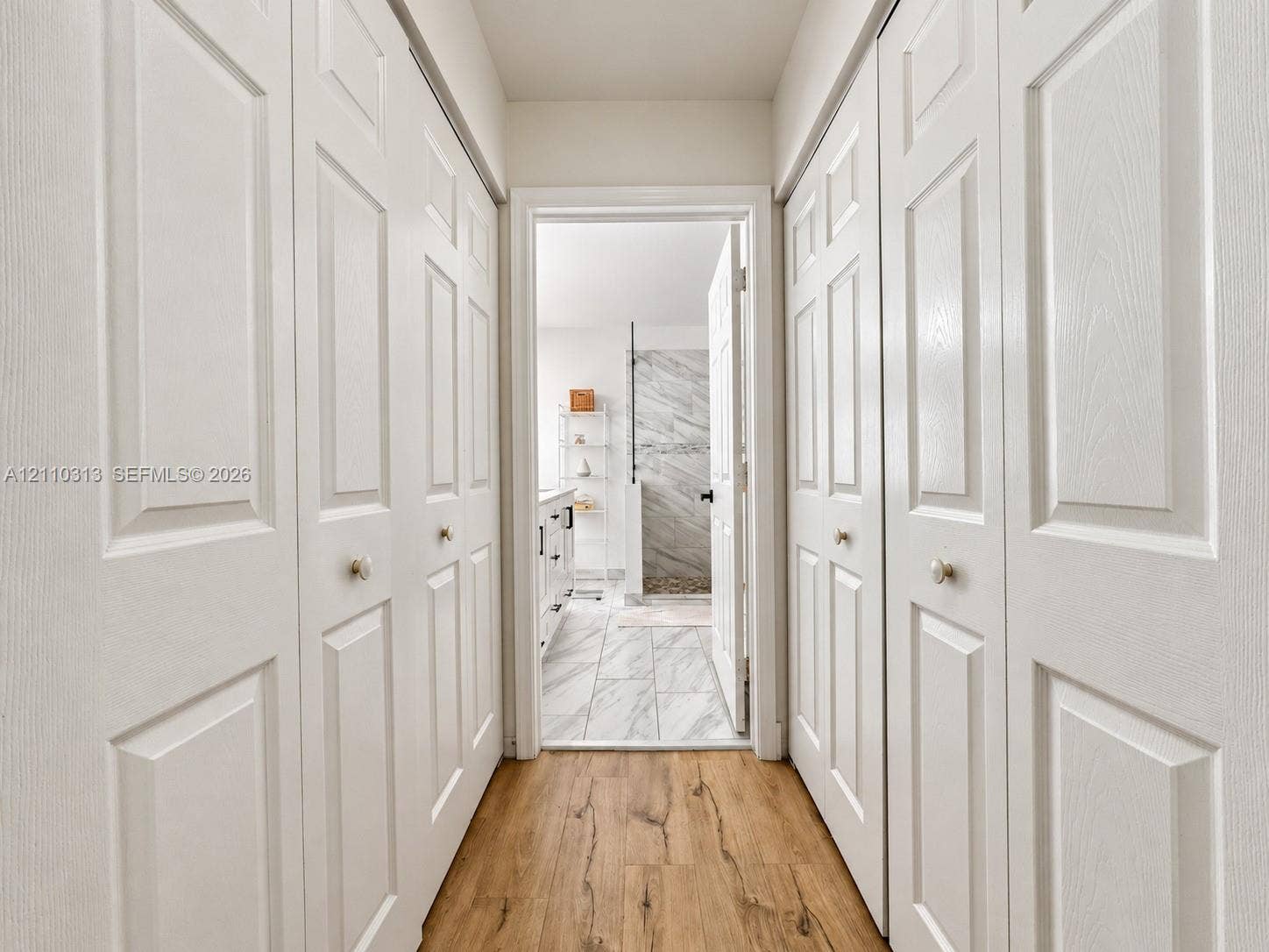 17731 SW 23rd Street, Miramar, FL 33029 Hallway featuring four white multi-panel bi-fold doors, wood-finish flooring, and stone-tile flooring in the interior space