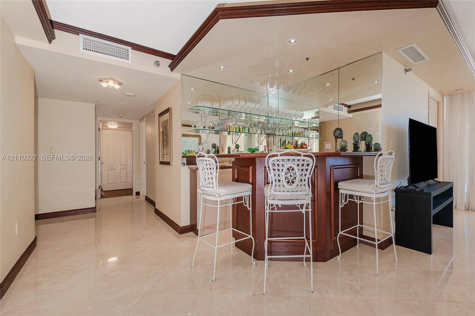 Custom wood-finish wet bar with a mirrored backsplash, glass shelving, recessed lighting, and tile flooring