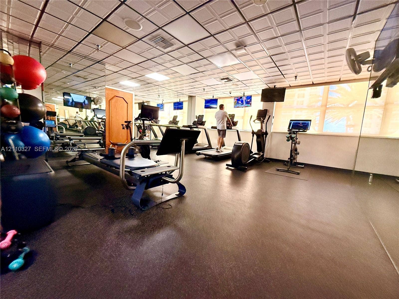 Fitness area featuring a coffered drop ceiling, expansive wall-to-wall mirrors, and durable rubberized flooring