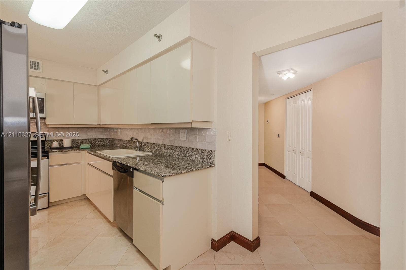 Kitchen featuring flat-panel cabinetry, light-toned stone countertops, a dark-finish double-door refrigerator, and polished stone tile flooring throughout