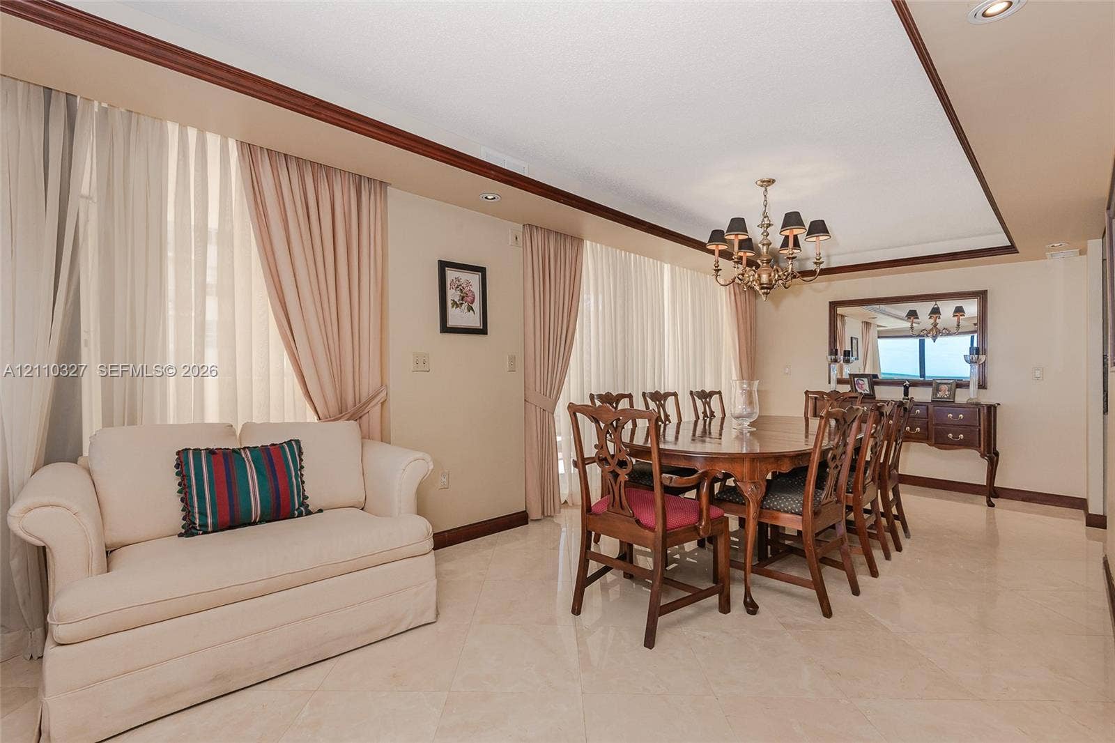 Curved architectural wall feature, polished stone-finish tile flooring, custom tiered wood crown molding, and ornate multi-arm chandelier