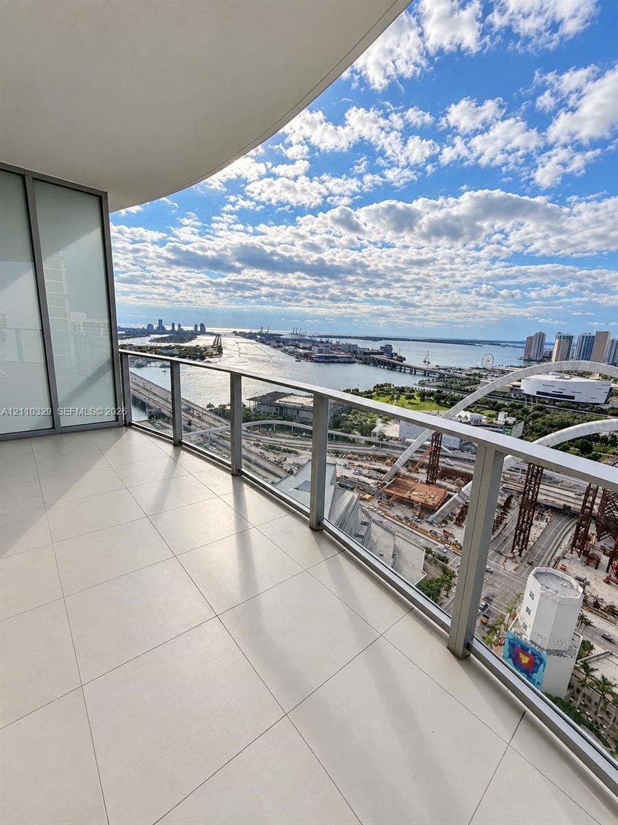 Covered balcony featuring large-format porcelain tile flooring and a glass panel railing