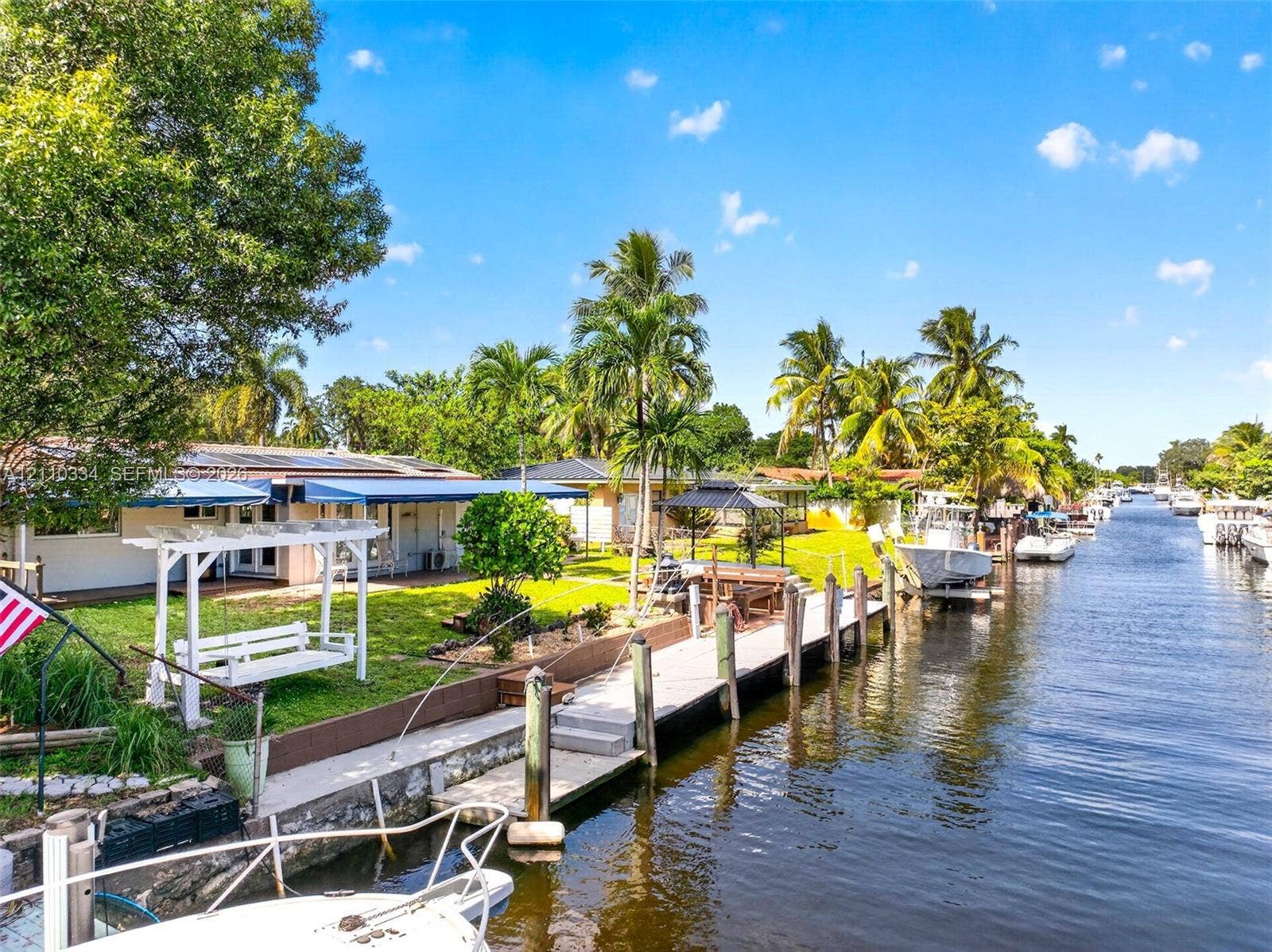 2100 SW 23rd Terrace, Fort Lauderdale, FL 33312 Waterfront property featuring a private concrete boat dock, seawall, landscaped lawn, and retractable exterior awnings