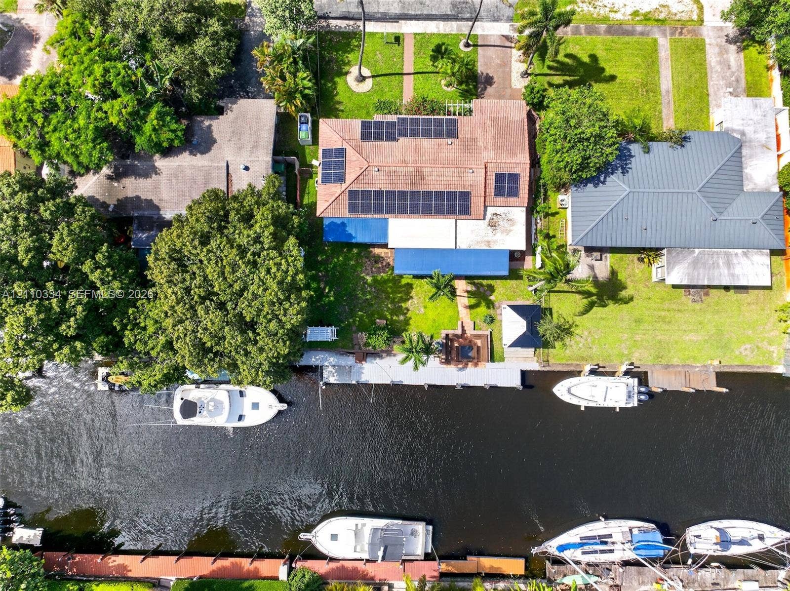 2100 SW 23rd Terrace, Fort Lauderdale, FL 33312 Waterfront property featuring a private dock, solar panel array, tiled roof, mature landscaping, and bulkhead retaining wall