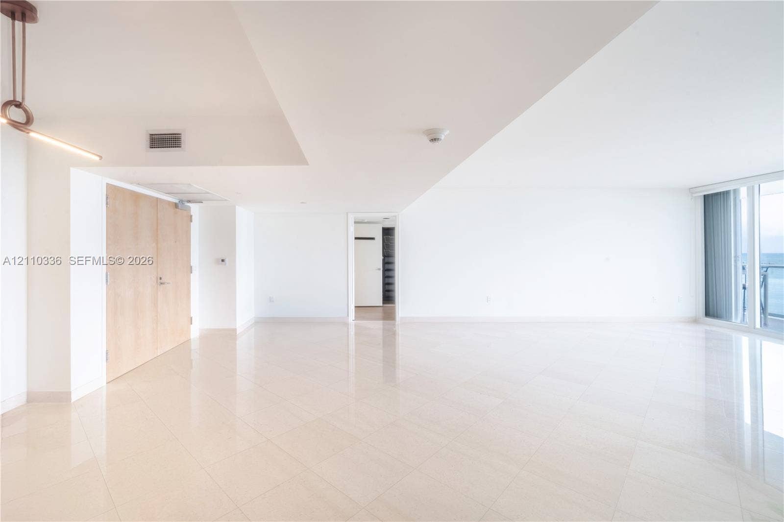 16445 Collins Avenue, #WS-7B, Sunny Isles Beach, Sunny Isles Beach, FL 33160 Open-concept interior featuring light-toned tile flooring, floor-to-ceiling windows, natural finish wood doors, and a contemporary linear pendant light fixture