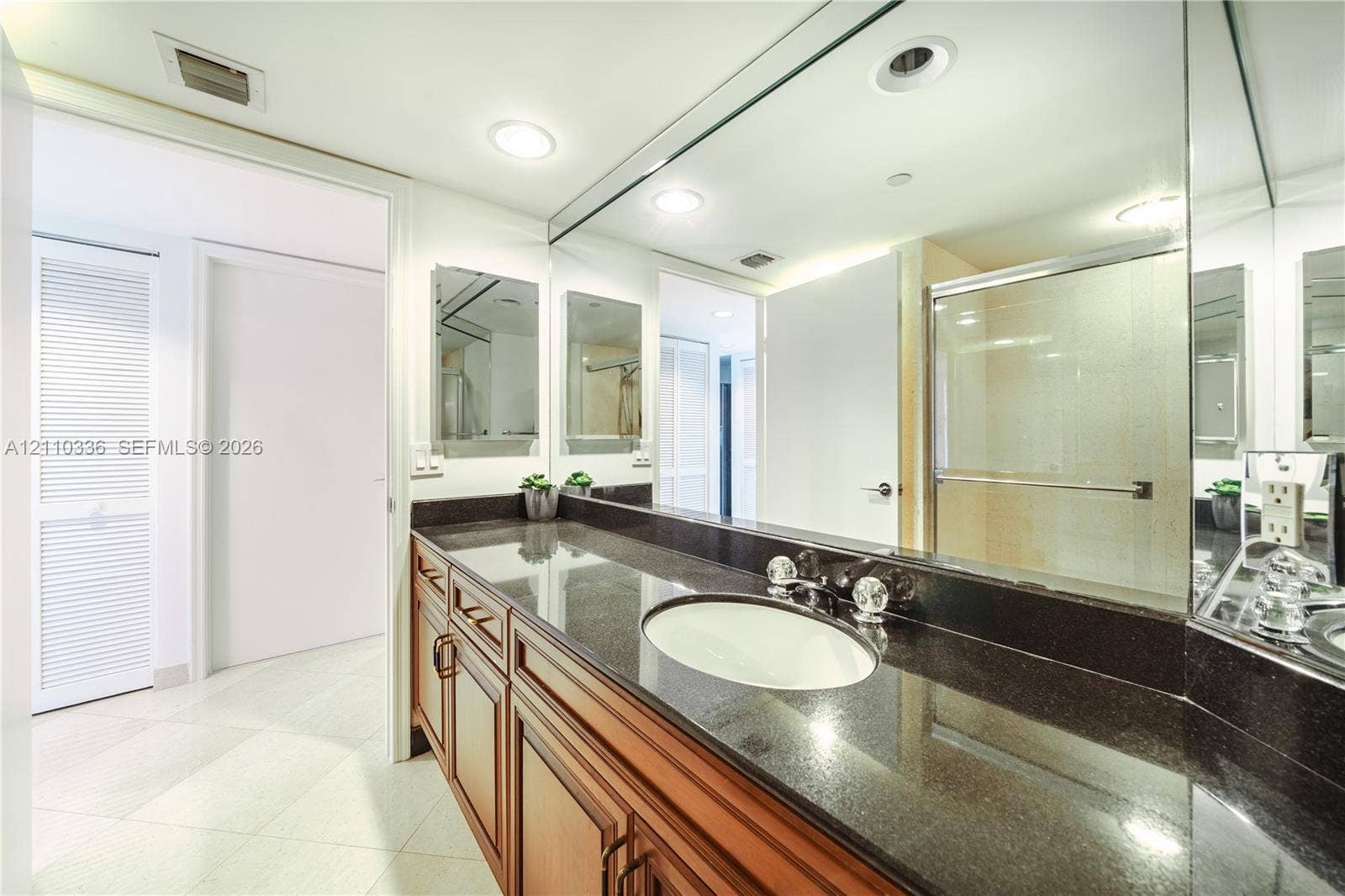 16445 Collins Avenue, #WS-7B, Sunny Isles Beach, Sunny Isles Beach, FL 33160 Vanity featuring a dark stone countertop, an integrated oval basin, warm-toned wood cabinetry, a full-width wall mirror, and recessed lighting