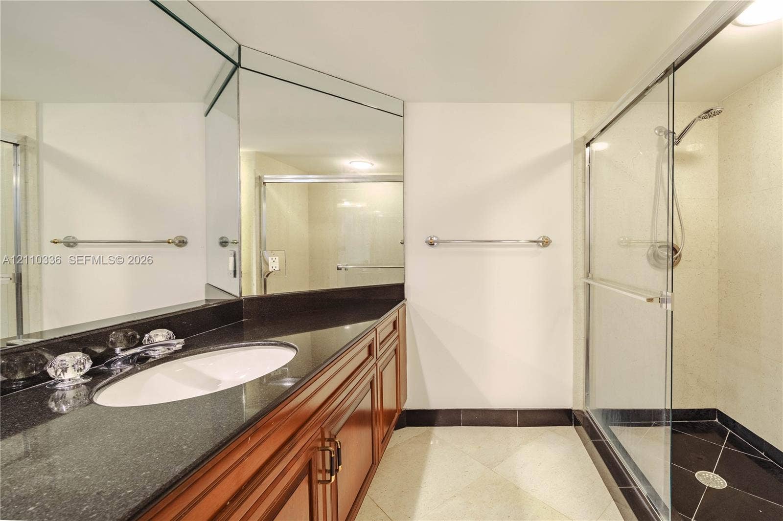 16445 Collins Avenue, #WS-7B, Sunny Isles Beach, Sunny Isles Beach, FL 33160 Vanity with dark countertop and white oval under-mount sink, wood-finish cabinetry, floor-to-ceiling mirror, and glass-enclosed shower with tiled flooring