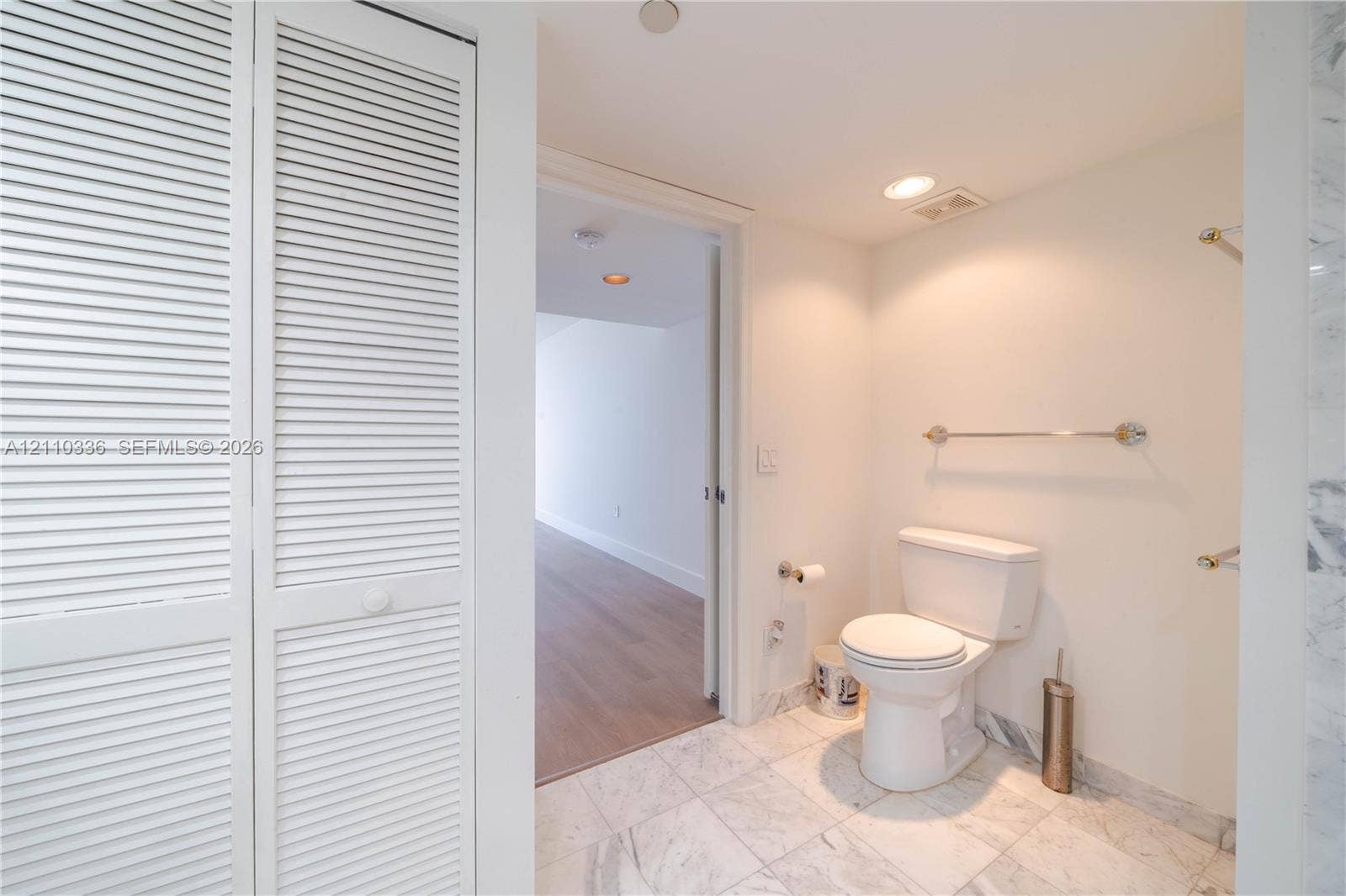 16445 Collins Avenue, #WS-7B, Sunny Isles Beach, Sunny Isles Beach, FL 33160 Bathroom featuring white louvered closet doors, stone-patterned tile flooring, a standard-profile toilet, and polished metal wall-mounted towel bars