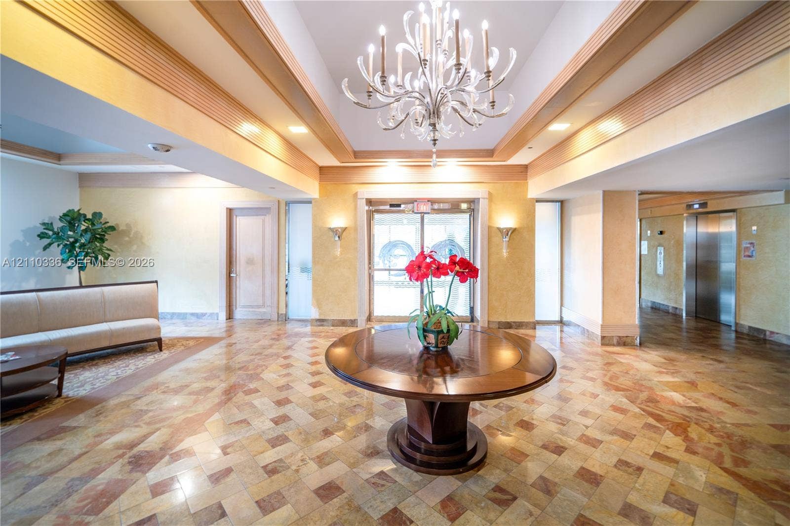 16445 Collins Avenue, #WS-7B, Sunny Isles Beach, Sunny Isles Beach, FL 33160 Grand foyer featuring a coffered ceiling with a multi-tiered crystal chandelier, intricate stone tile flooring, and integrated wall sconces