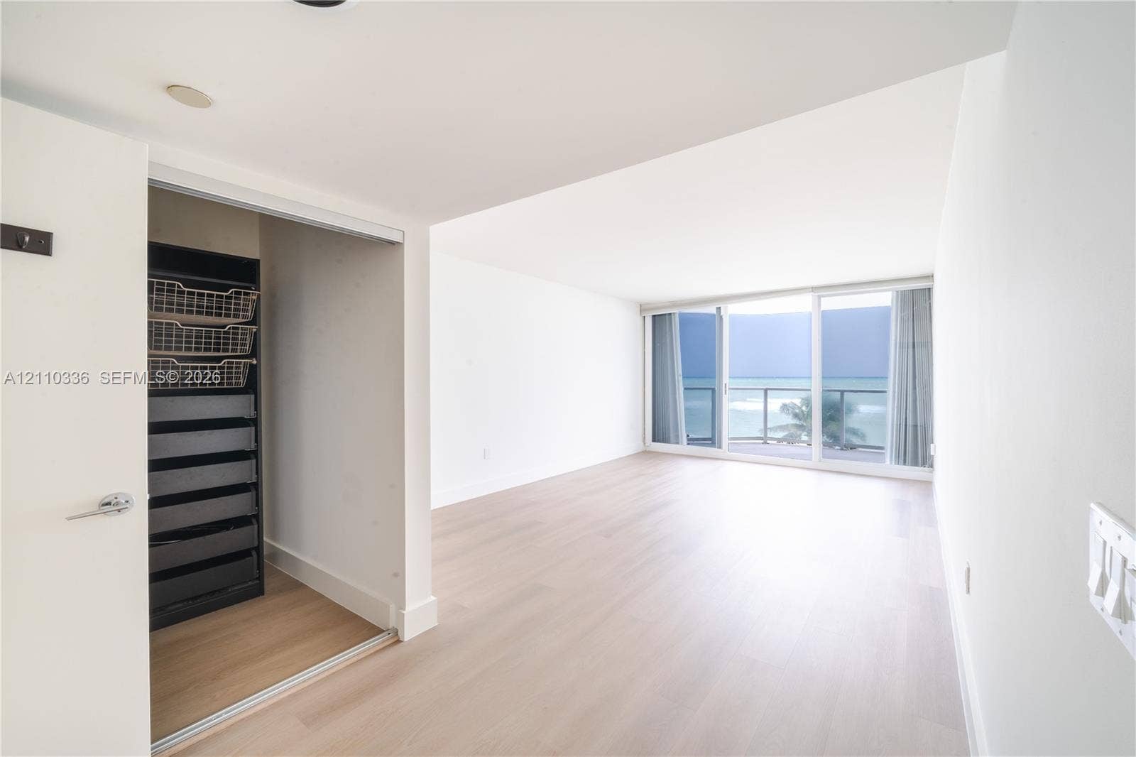 16445 Collins Avenue, #WS-7B, Sunny Isles Beach, Sunny Isles Beach, FL 33160 Living area featuring light wood-finish flooring, floor-to-ceiling sliding glass doors, built-in closet organization system, and ocean horizon backdrop