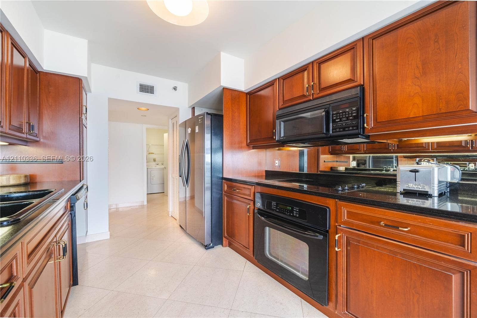 16445 Collins Avenue, #WS-7B, Sunny Isles Beach, Sunny Isles Beach, FL 33160 Kitchen featuring warm-toned wood cabinetry, dark stone countertops, mirror backsplash, stainless steel appliances, and tile flooring