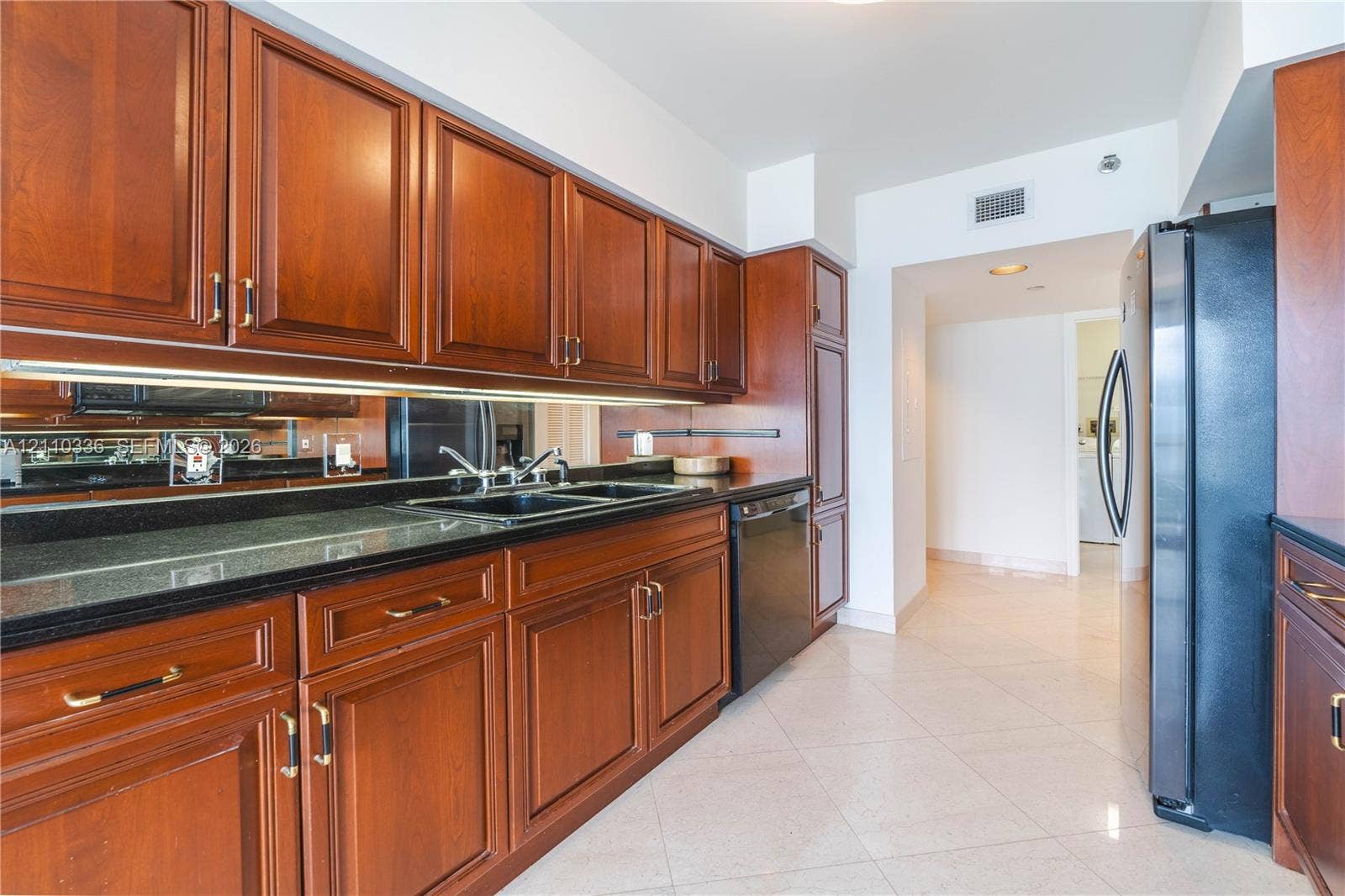 16445 Collins Avenue, #WS-7B, Sunny Isles Beach, Sunny Isles Beach, FL 33160 Kitchen featuring raised-panel wood cabinetry, black countertops, mirrored backsplash, under-cabinet lighting, and black appliances