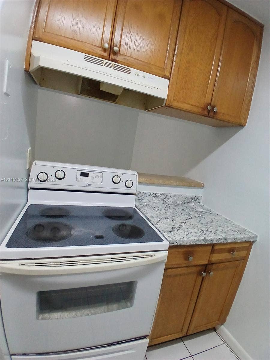 Kitchen featuring wood cabinetry, stone-finish countertops, and a white electric range with a built-in hood
