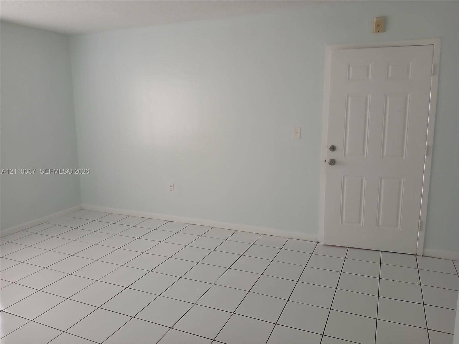 Interior room featuring large-format square tile flooring, neutral wall paint, and a six-panel entry door with metallic hardware